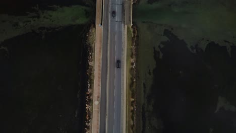 Reveal-shot-cars-on-bridge-road-across-the-lagoon-toward-the-old-island-town-Orbetello-close-to-Monte-Argentario-and-the-Maremma-Park-in-Tuscany,-Italy,-with-water-reflections