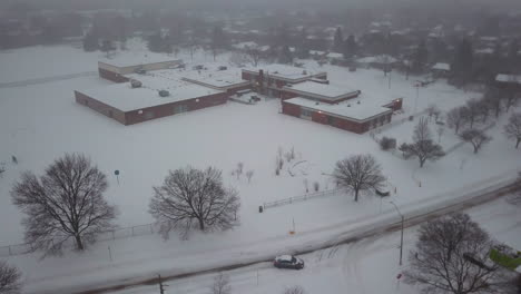Winter-aerial-view-of-a-snow-covered-school-in-a-residential-community