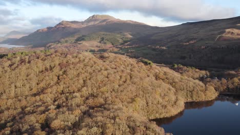 Aerial-drone-footage-of-an-autumn-sunrise-over-Loch-Lomond-and-Ben-Lomond-mountain-in-the-Loch-Lomond-and-the-Trossachs-National-Park-in-Scotland-with-native-broadleaf-woodland-in-the-foreground