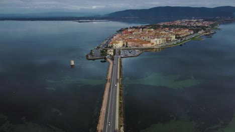 Cars-on-bridge-road-across-the-lagoon-toward-the-old-island-town-Orbetello-close-to-Monte-Argentario-and-the-Maremma-Nature-Park-in-Tuscany,-Italy,-with-water-reflections