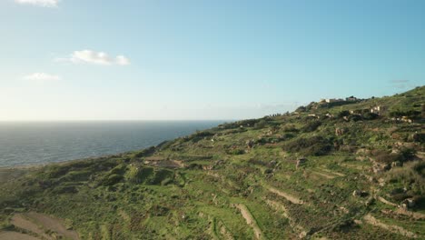 AERIAL:-Car-Driving-up-to-Hill-near-Mediterranean-Sea-on-a-Sunny-Evening-in-Malta
