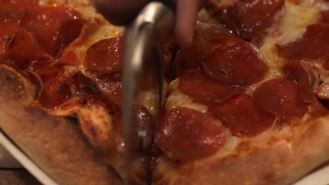 Using-a-pizza-wheel-to-slice-a-freshly-baked-homemade-pepperoni-pizza-into-servings---isolated-close-up