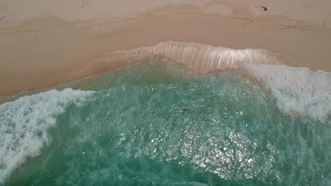 Blue-waves-crashing-into-a-prestine-beach,-top-down-view-from-a-drone
