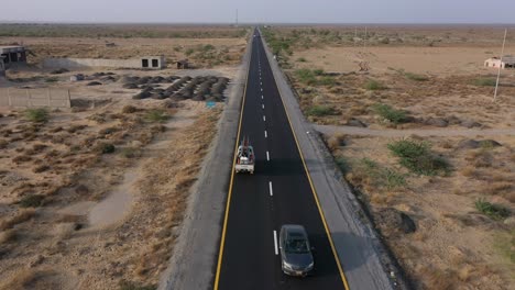 Antenne-über-Der-Straße-Durch-Wüstenebenen-In-Belutschistan-Mit-Geparktem-LKW-Und-Vorbeifahrenden-Autos