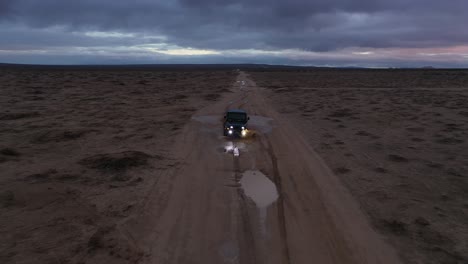 Driving-a-jeep-through-the-Mojave-Desert-just-after-a-heavy-rain-at-sunset-with-a-colorful-sky---aerial-view