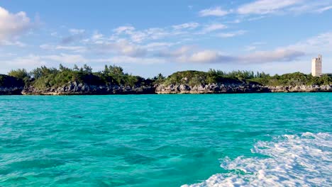 Sailing-with-a-boat-in-the-turquoise-ocean-water-near-the-rocky-shore-of-Blue-Lagoon-Island,-Bahamas