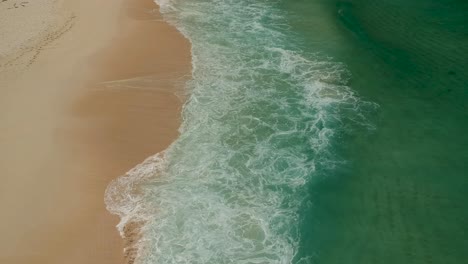 Waves-breaking-onto-a-beach-as-view-from-above,-shot-with-a-drone-at4K