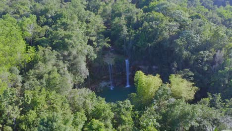 Aerial-backwards-shot-of-tropical-waterfall-surrounded-by-dense-tropical-forest-trees-in-summer---Salto-Alto,Bayaguana