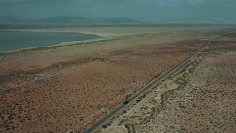 Aerial-Over-Following-Behind-Car-Travelling-Along-Road-Through-Desert-Plains-In-Balochistan