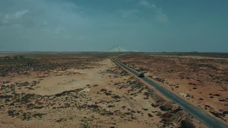 Vista-Aérea-Del-Coche-Que-Viaja-A-Lo-Largo-De-La-Carretera-A-Través-De-Las-Llanuras-Del-Desierto-En-Baluchistán
