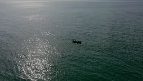 Aerial-View-Of-Silhouette-Of-Boat-Floating-In-Arabian-Sea-With-Sunlight-Reflection
