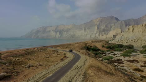 Aerial-Tracking-View-Of-4x4-Truck-Driving-Along-Road-Beside-Coastline-In-Balochistan