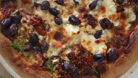 Overhead-sliding-view-of-freshly-baked-combination-pizza-with-black-olives,-tomatoes,-peppers-and-other-ingredients-baked-in-the-cheese