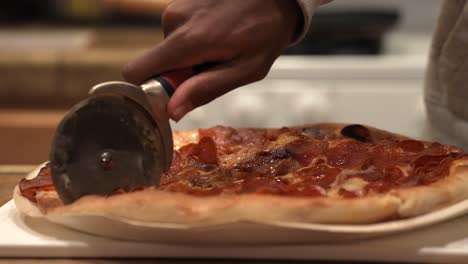 Aufschneiden-Einer-Frisch-Gebackenen-Peperoni-Pizza-Mit-Einem-Pizzarad-Heiß-Aus-Dem-Ofen---Seitenansicht