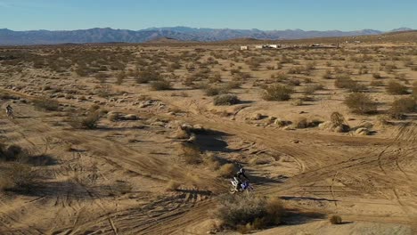Motociclistas-Disfrutando-De-Una-Aventura-Fuera-De-La-Carretera-En-El-Escarpado-Desierto-De-Mojave-Con-Salto-Alto---Vista-Aérea-En-Cámara-Lenta