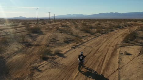 Off-road-motorcyclist-riding-down-a-dirt-road-in-the-Mojave-Desert---slow-motion-aerial-view