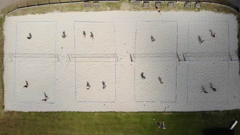 Aerial:-Drone-top-down-view-of-beach-volley-pit-while-people-are-playing-games-on-4-tracks-on-a-hot-summer-day-in-4k