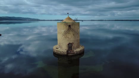 Old-Spanish-windmill-in-the-lagoon-at-old-island-town-Orbetello-near-Monte-Argentario-and-the-Maremma-Nature-Park-in-Tuscany,-Italy,-with-blue-sky-and-calm-blue-water