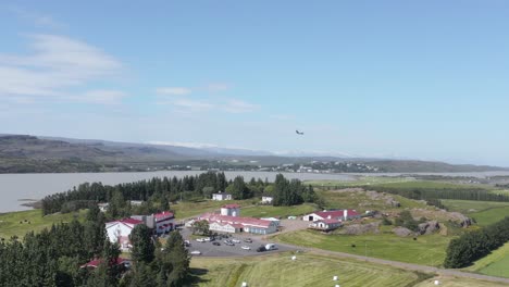 Lake-Hotel-Egilsstaðir-with-airplane-passing-by-landing-on-nearby-airstrip,-aerial