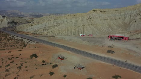 Antena-De-Carretera-Vacía-Y-Parada-De-Camiones-Rodeada-De-Colinas-Erosionadas-En-El-Parque-Nacional-Hingol-En-Baluchistán