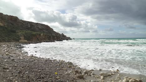Piles-of-Rocks-On-a-Golden-Bay-Beach-with-Mediterranean-Sea-Waves-Crashing-on-Sandy-Shore