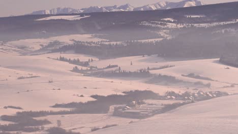 Slow-tilt-up-over-beautiful-snow-covered-landscape-with-small-villages,-forests-and-mountains