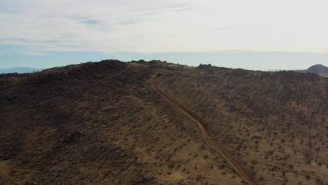 All-terrain-vehicle-climbing-a-steep-incline-to-the-top-to-reveal-the-vast-Mojave-Desert-landscape---aerial-view
