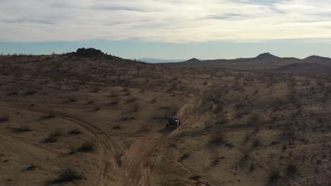 An-all-terrain-vehicle-climbing-a-incline-to-a-high-plateau-in-the-Mojave-Desert-and-a-view-of-the-surrounding-rugged-terrain---aerial-view