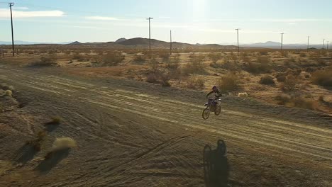 Motorcycle-rider-jumping-across-a-road-in-the-Mojave-Desert-in-slow-motion---aerial-view