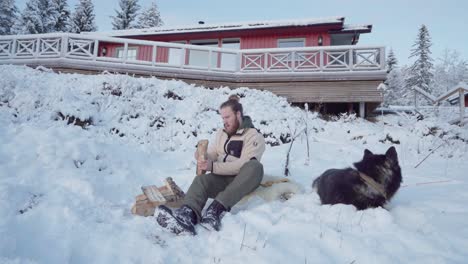 Mann-Und-Sein-Hund-Sitzen-Im-Winter-Auf-Schnee-Neben-Einem-Holzstapel