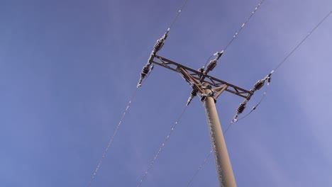 Looking-up-at-utility-pole-with-snow-falling-off-against-blue-sky