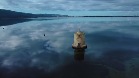 Old-Spanish-mill-in-the-lagoon-at-old-island-town-Orbetello-near-Monte-Argentario-and-the-Maremma-Nature-Park-in-Tuscany,-Italy,-with-blue-sky-and-calm-blue-water