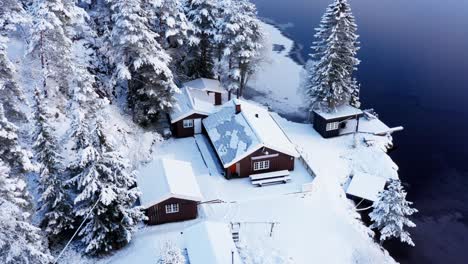 Scenic-View-Of-Cabins-By-The-Lakeshore-In-Snowscape-During-Winter