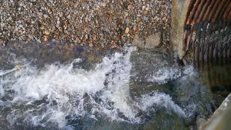 Wasser-Aus-Einem-Abfluss-In-Einer-Steinmauer-über-Einen-Steinigen-Strand-In-Broad-Haven,-Westwales