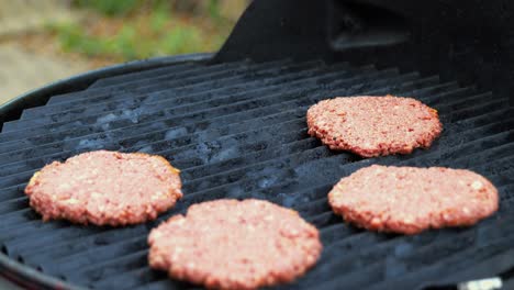 Placing-seasoned-raw-Plant-Based-Impossible-Meat-Burger-patties-on-electric-grill-with-metal-spatula-at-outdoor-barbecue-at-home---in-Cinema-4k-