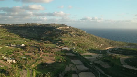 AERIAL:-Flying-Above-Green-Farm-Lands-near-Coastline-of-Malta-in-Winter-During-Golden-Hour
