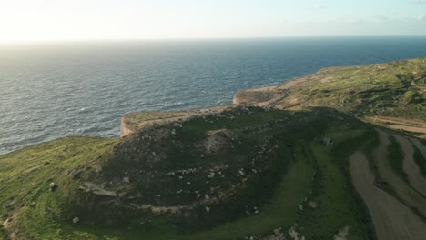 AERIAL:-Reveal-Shot-of-Rocky-Green-Hill-near-Mediterranean-Sea-In-Malta