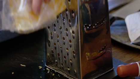 Block-of-Colby-Jack-Cheddar-Cheese-being-grated-by-caucasian-white-hand-on-steel-metal-aluminum-queso-grater---in-Cinema-4k-