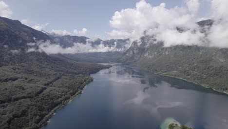 Video-Con-Un-Dron-De-Espalda-Plana-Sobre-El-Lago-Bohinj-Avanzando-Hacia-Su-Interior-Entre-Las-Montañas,-El-Cielo-Está-Despejado-Con-Algunas-Nubes