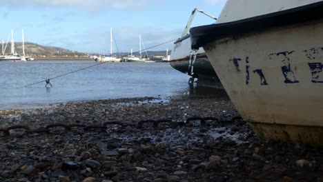 Leaking-boat-moored-on-pebble-beach-with-rusty-chain-at-low-tide