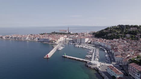 Video-with-a-flat-back-drone-on-the-coast-of-Piran-in-Slovenia,-shows-the-church-and-the-port,-discovering-the-promenade-that-gives-access-to-the-city,-you-can-see-the-circulation-of-vehicles