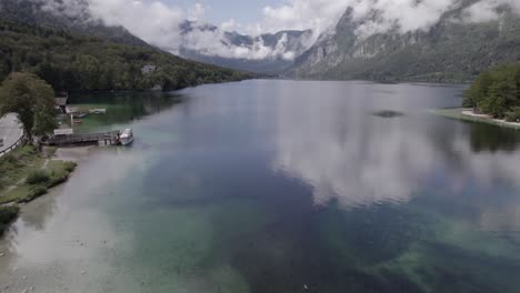 Front-descriptive-panning-drone-video-on-Lake-Bohinj-passing-over-the-Most-bridge-with-people-and-vehicles-circulating,-ending-with-the-horizon-in-the-mountains