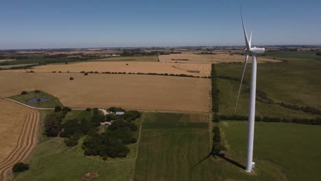 Aerial-orbiting-shot-of-rotating-wind-turbine-on-countryside-field-during-sunlight-and-blue-sky---Production-of-wind-energy-in-nature