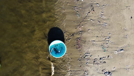 Schwimmende-Einweg-Plastiktüten-Und-Reisboote,-Die-Auf-Den-Langsam-Rollenden-Wellen-Am-Verschmutzten-Strand-Plätschern,-Während-Ein-Hund-Und-Sein-Besitzer-In-Vietnam-Spazieren-Gehen