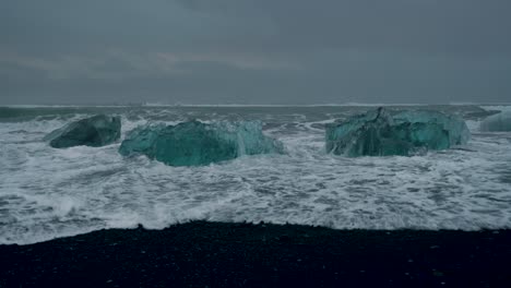 Epische-Statische-Aufnahme-Des-Isländischen-Jokulsarlon-strandes-Mit-Wellen,-Die-Massive-Eisberge-Während-Eines-Mystischen-Dunklen-Tages-überfluten