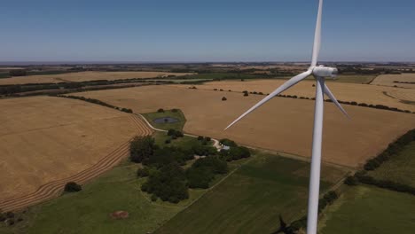 Aerial-orbit-shot-of-wind-turbine-production-of-sustainable-energy-surrounded-by-countryside-farm-fields-in-summer