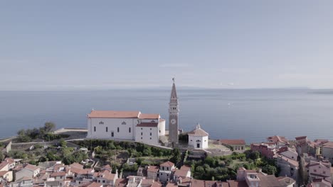 Video-with-drone-of-plane-backwards-over-the-city-of-Piran-in-Slovenia,-starting-with-the-Church-as-the-main-one-and-ending-from-overhead-at-the-marina-passing-through-the-central-square