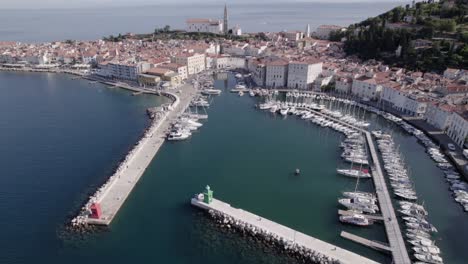 Descriptive-panning-drone-video-over-the-city-of-Piran-in-Slovenia,-you-can-see-the-port-with-the-boats-in-the-water-as-the-main-part-and-the-church-in-the-background