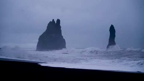 Wide-shot-of-Black-Beach-of-Reynisfjara-during-stormy-crashing-waves-and-mystical-basalt-boulders-in-Iceland