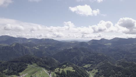 Frontal-drone-video-moving-over-houses-in-the-Triglav-with-hills-on-the-horizon,-and-clear-sky-with-clouds